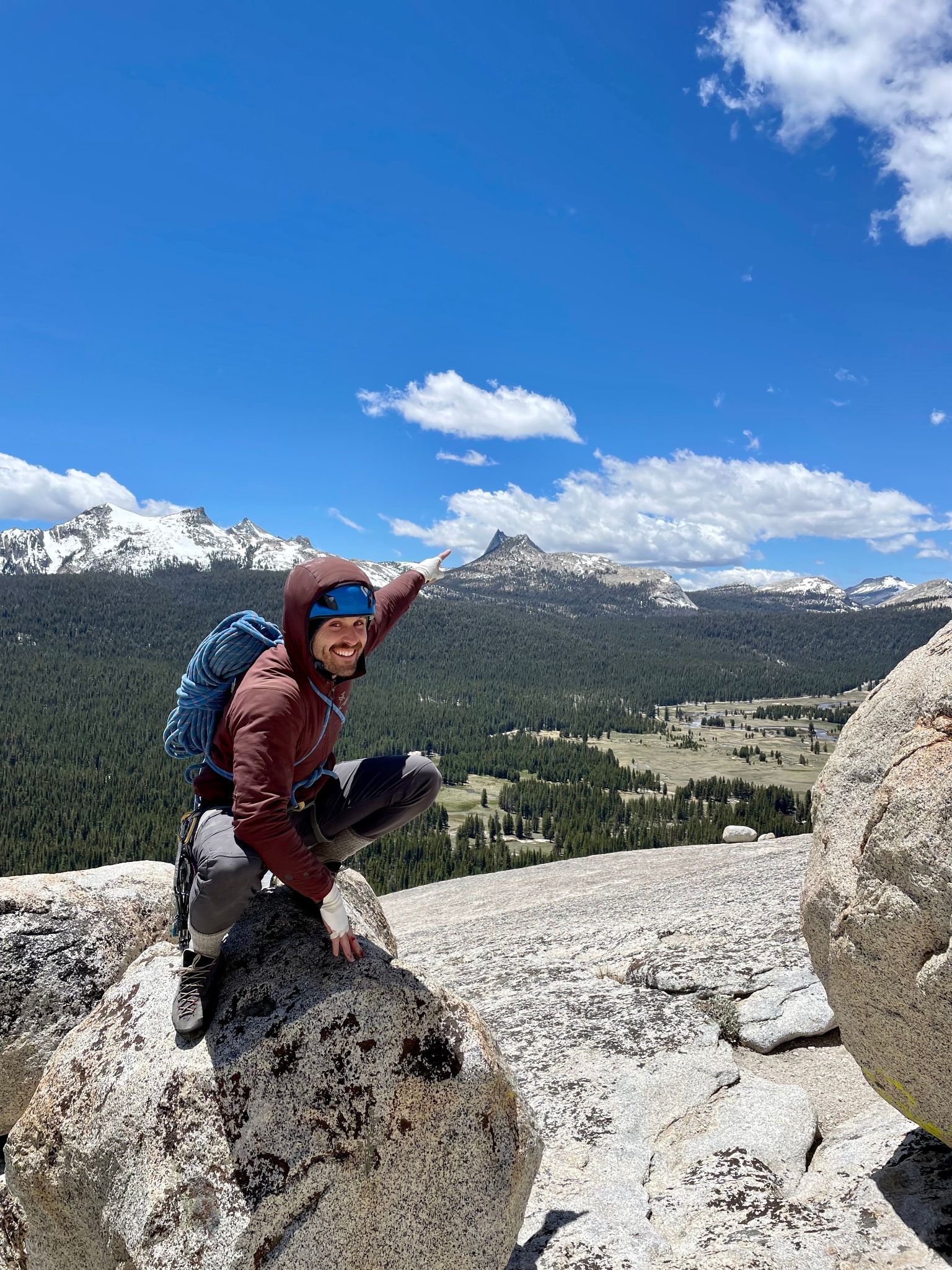 Kyle stands on top of a small cliff face with both arms raised in triumph, he is still tied into a rope